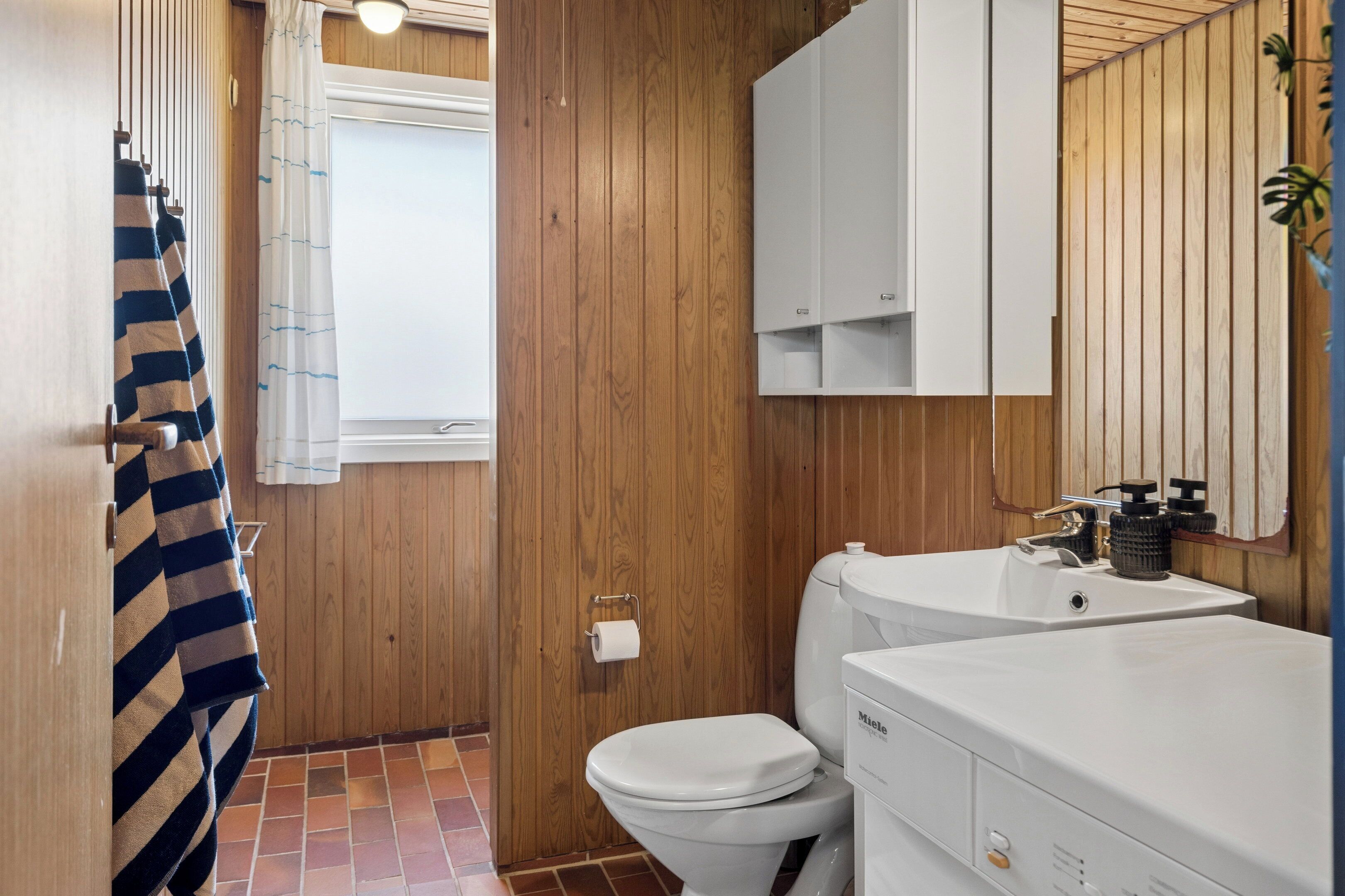 A bathroom with wooden paneling, a white toilet, a sink with a mirror, and a towel rack with striped towels.