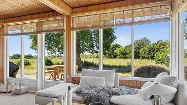 Ein modernes Wohnzimmer mit einer Couch, einem Couchtisch und Blick auf eine grüne Landschaft durch große Fenster.