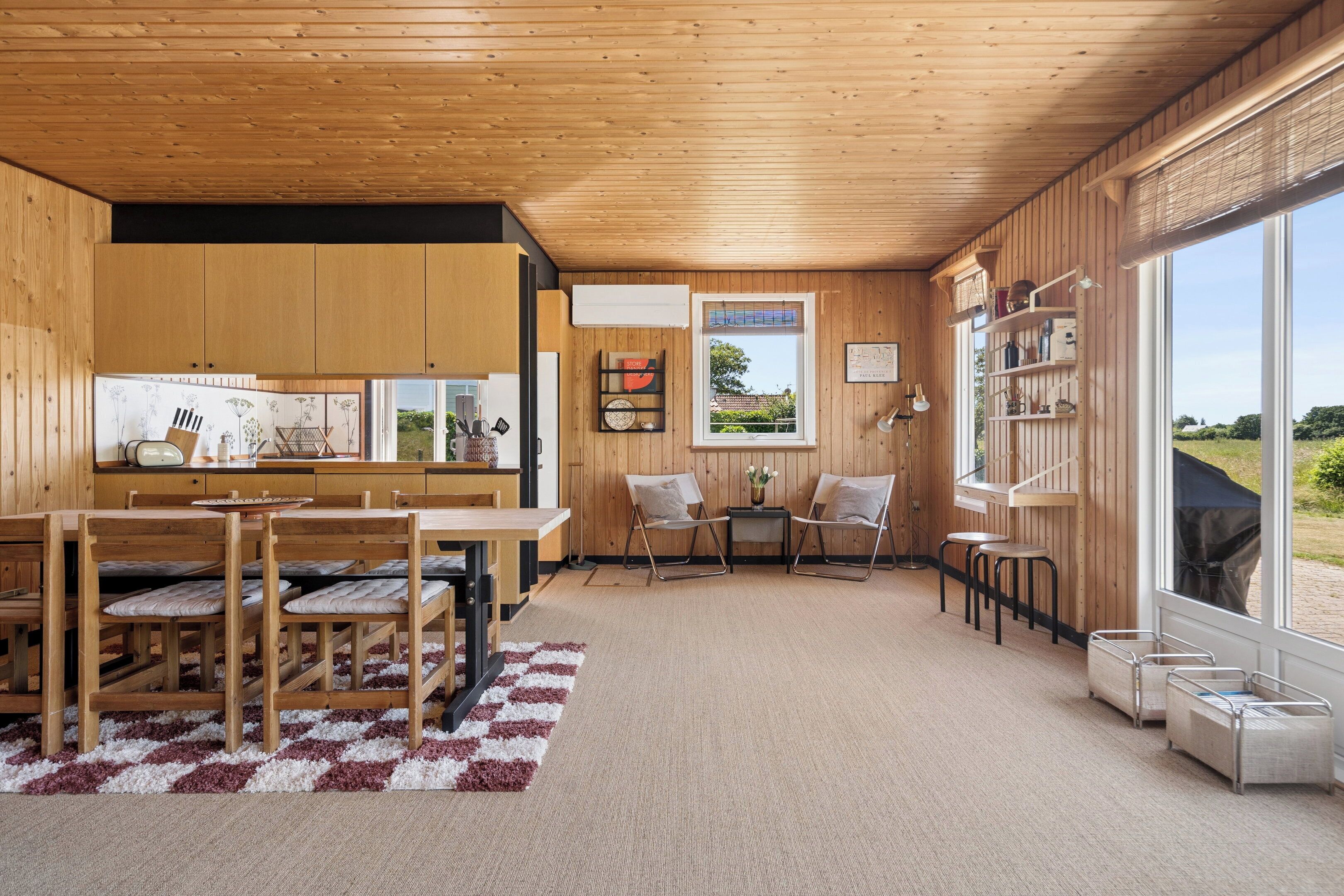 Una cucina moderna con mobili in legno, un'area pranzo con tappeto a scacchi e vista panoramica attraverso ampie finestre.