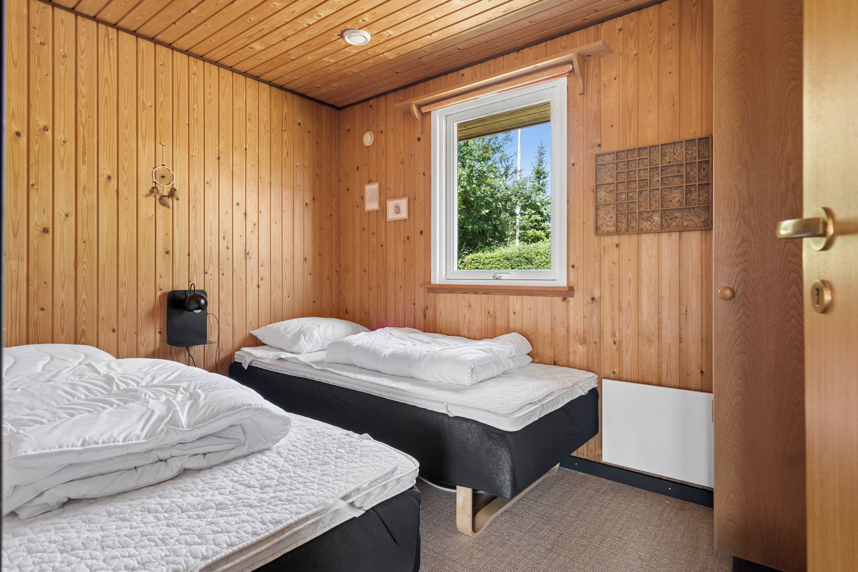 Ein Zimmer mit Holzwänden, zwei Betten, einem Fenster mit Blick ins Grüne und einem an der Wand befestigten Lautsprecher.
