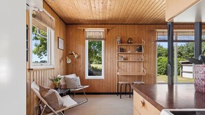Ein gemütlicher Holzraum mit Küchenzeile, einem Klappstuhl, einem kleinen Tisch und einem Fenster mit Blick auf Grünflächen.