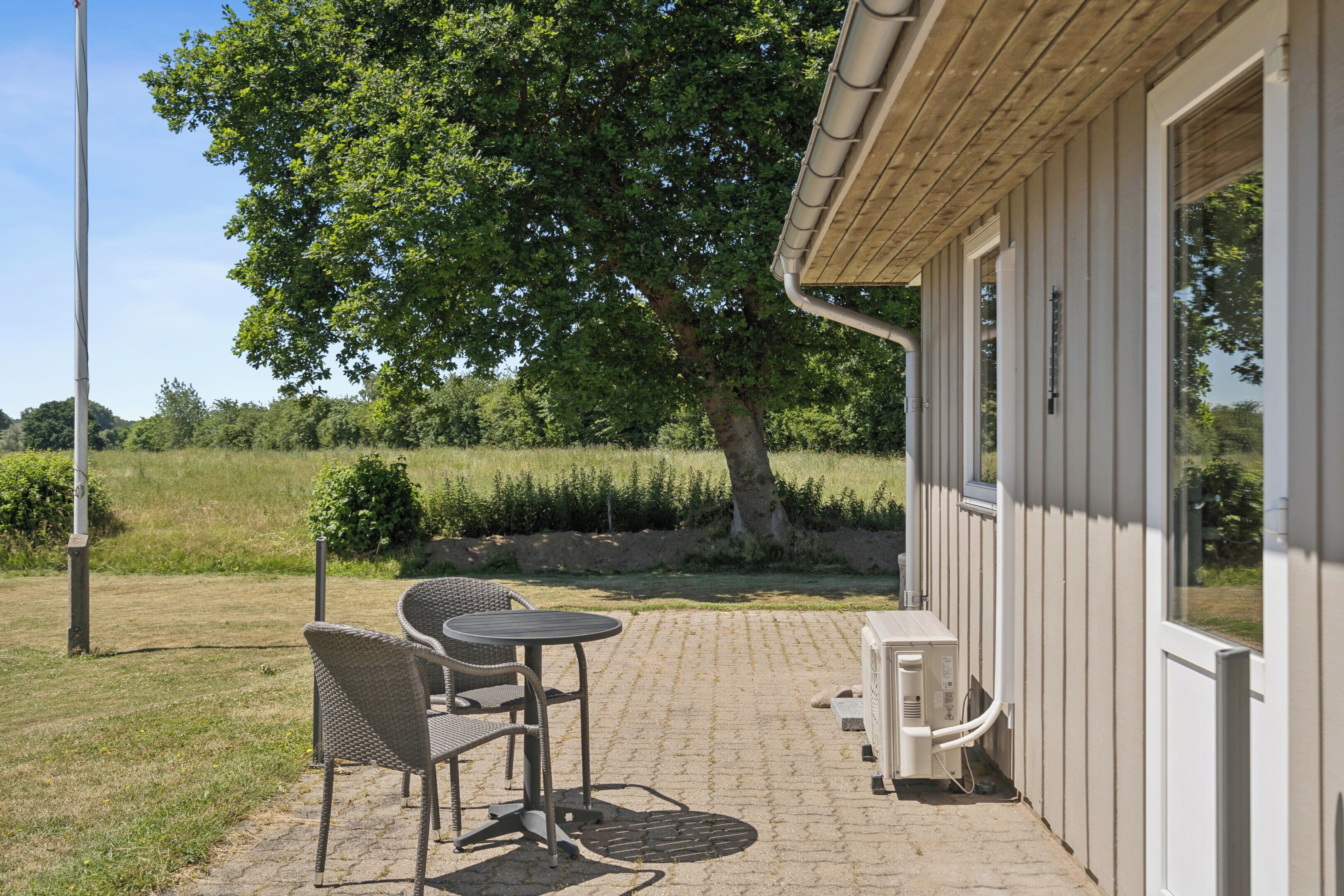 A patio with wicker chairs and a table, a tree, and a building with large windows.