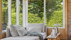 Ein Zimmer mit einer Sitzecke, einem kleinen Tisch und Blick auf Grün durch große Fenster.