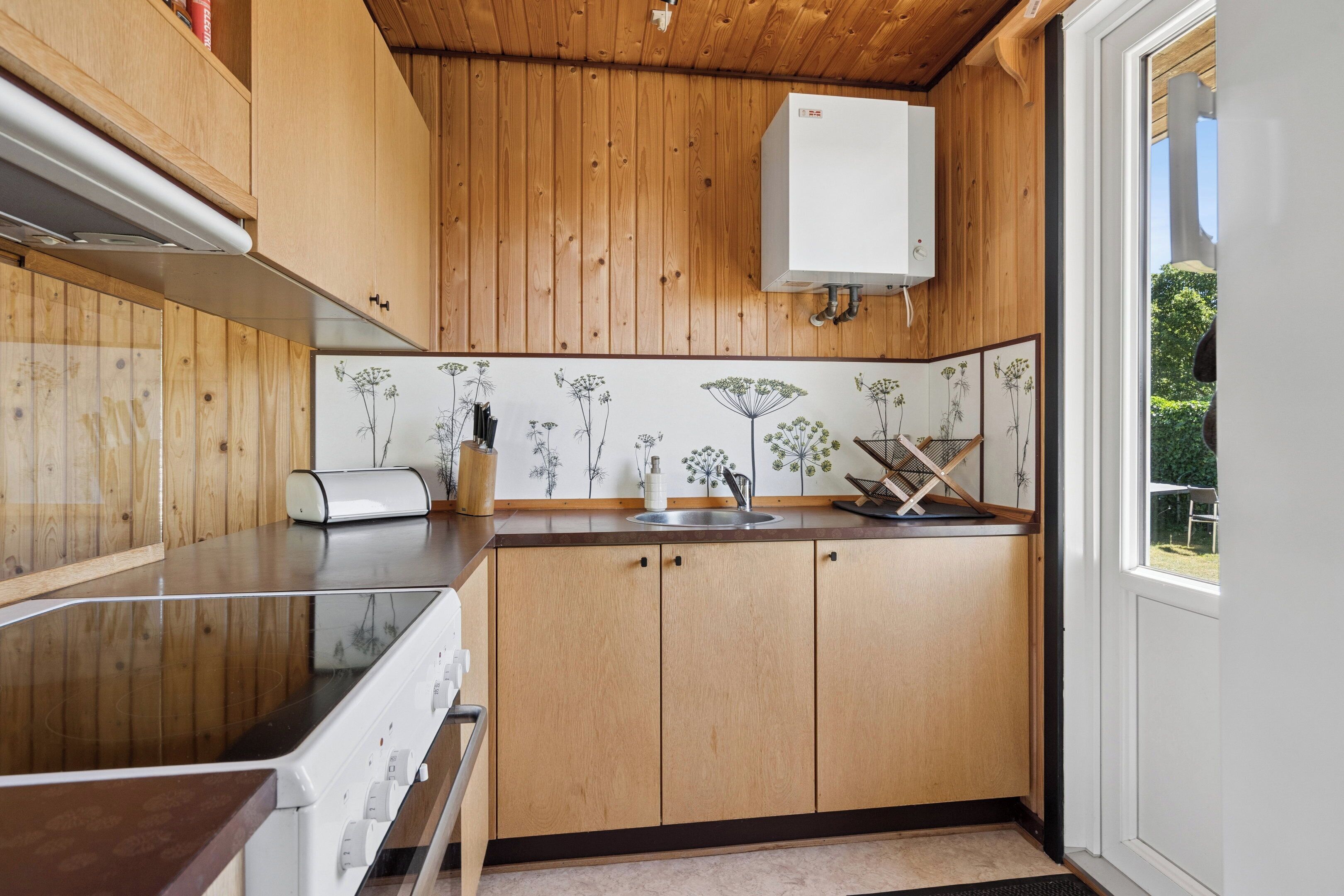 A kitchen with wooden cabinets, a white countertop, and a window with a view of greenery.