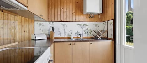 A kitchen with wooden cabinets, a white countertop, and a window with a view of greenery.