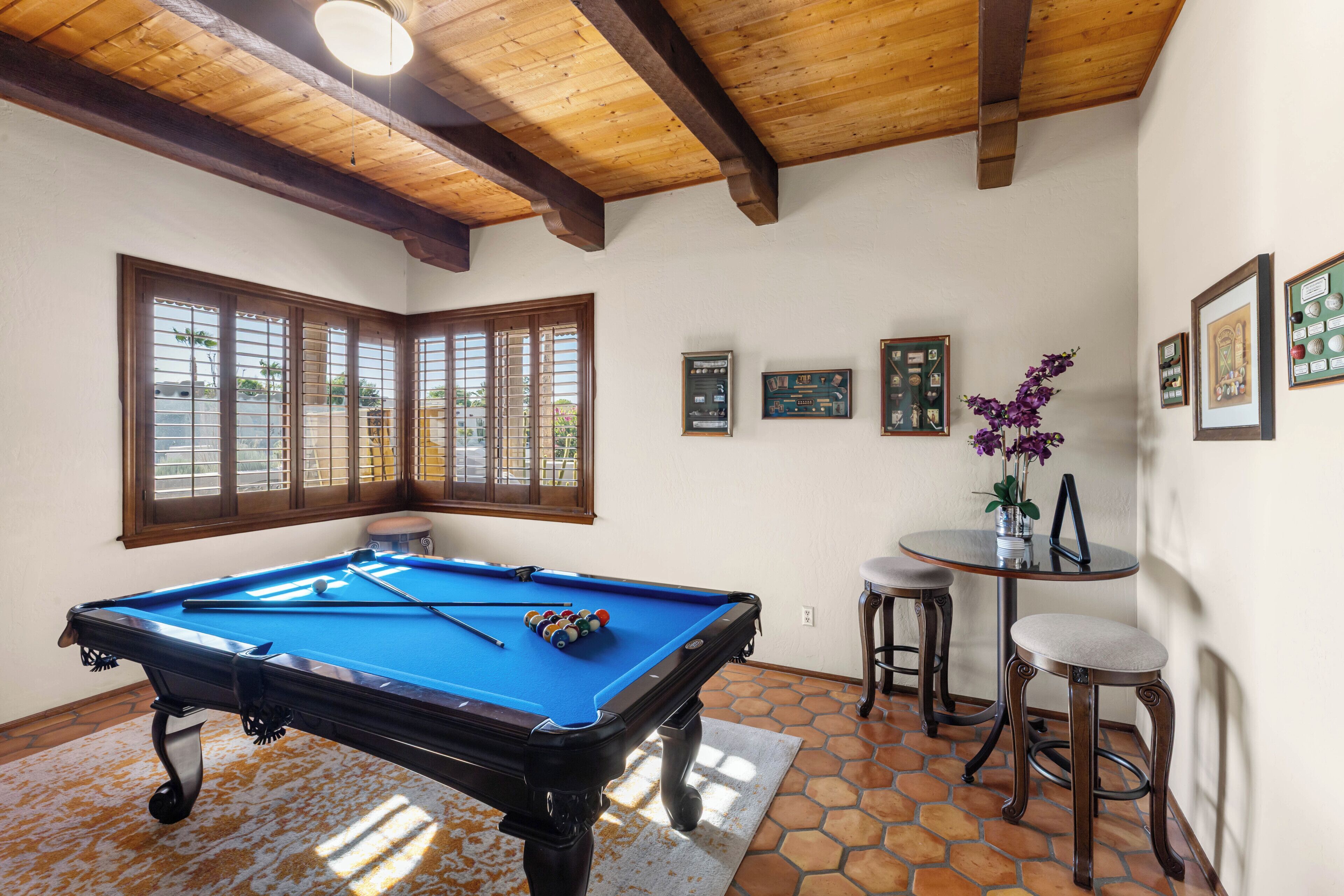 A pool table with a blue felt surface, wooden beams on the ceiling, and a tiled floor.