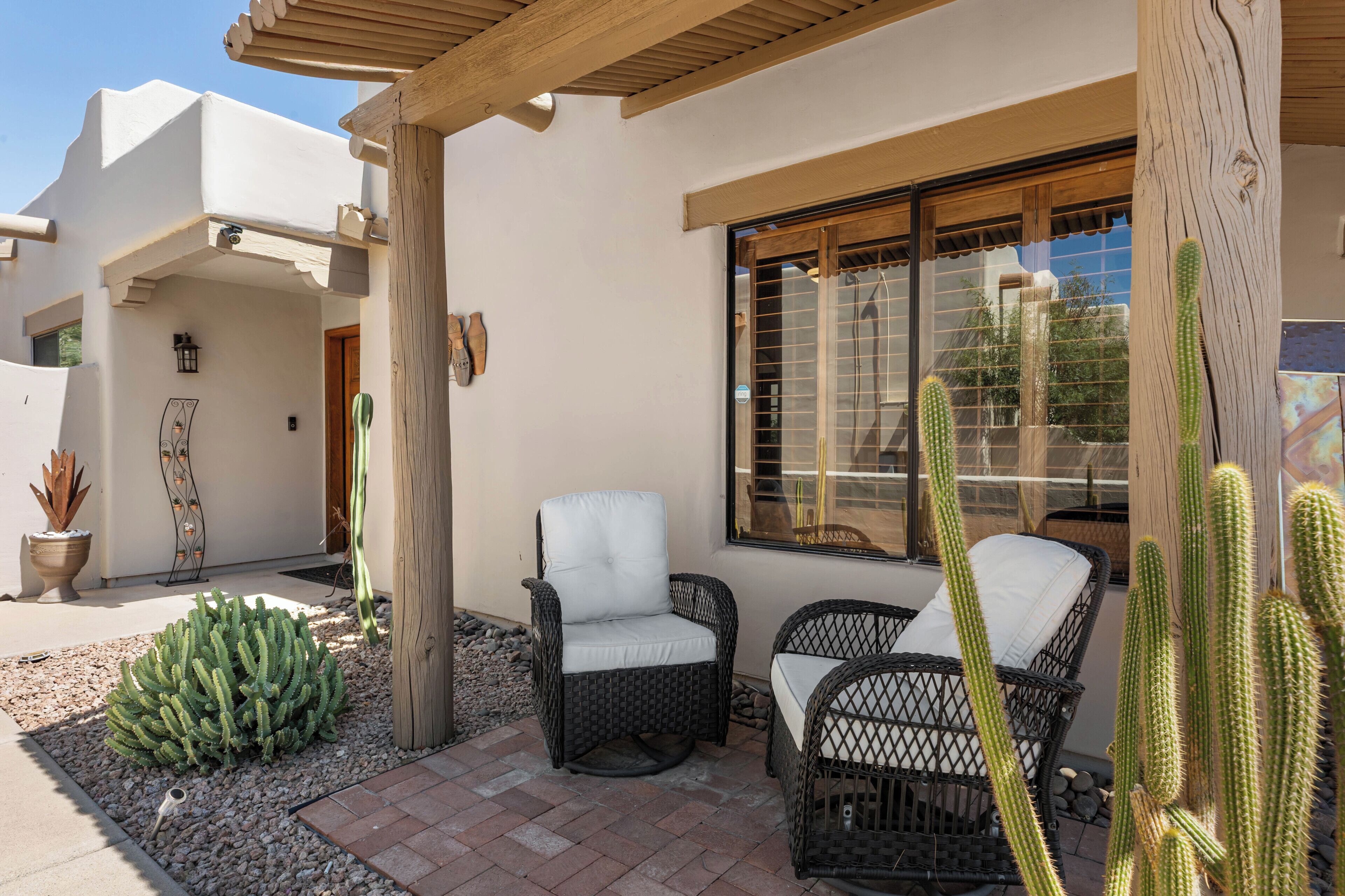 Une terrasse dotée de meubles en osier, un jardin de cactus et un bâtiment agrémenté d’une pergola en bois.