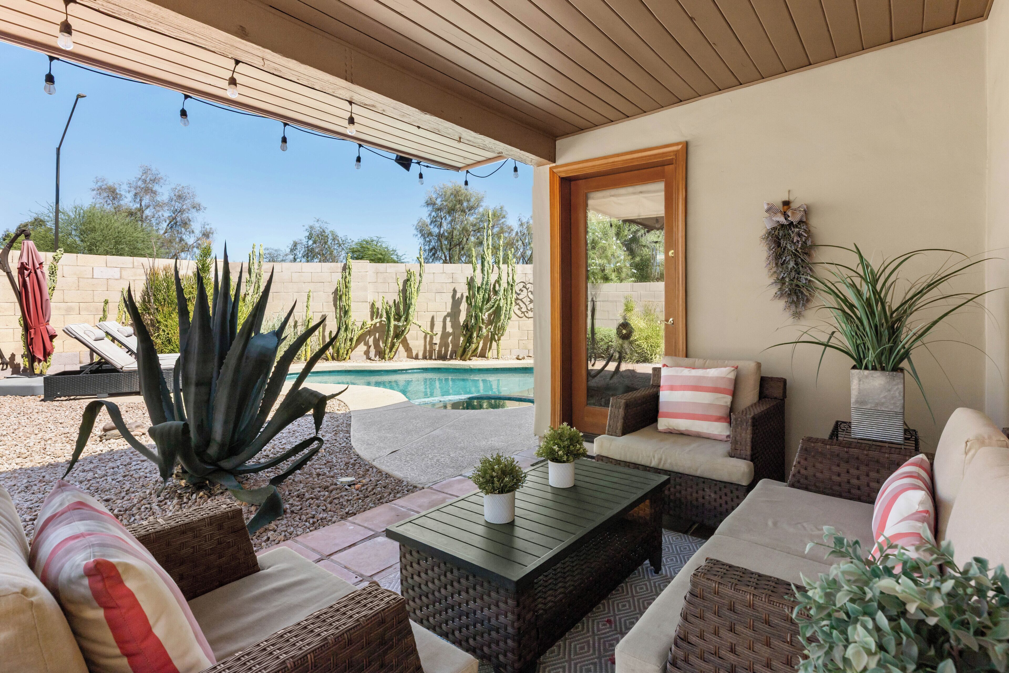 An outdoor patio with a pool, wicker furniture, and potted plants.