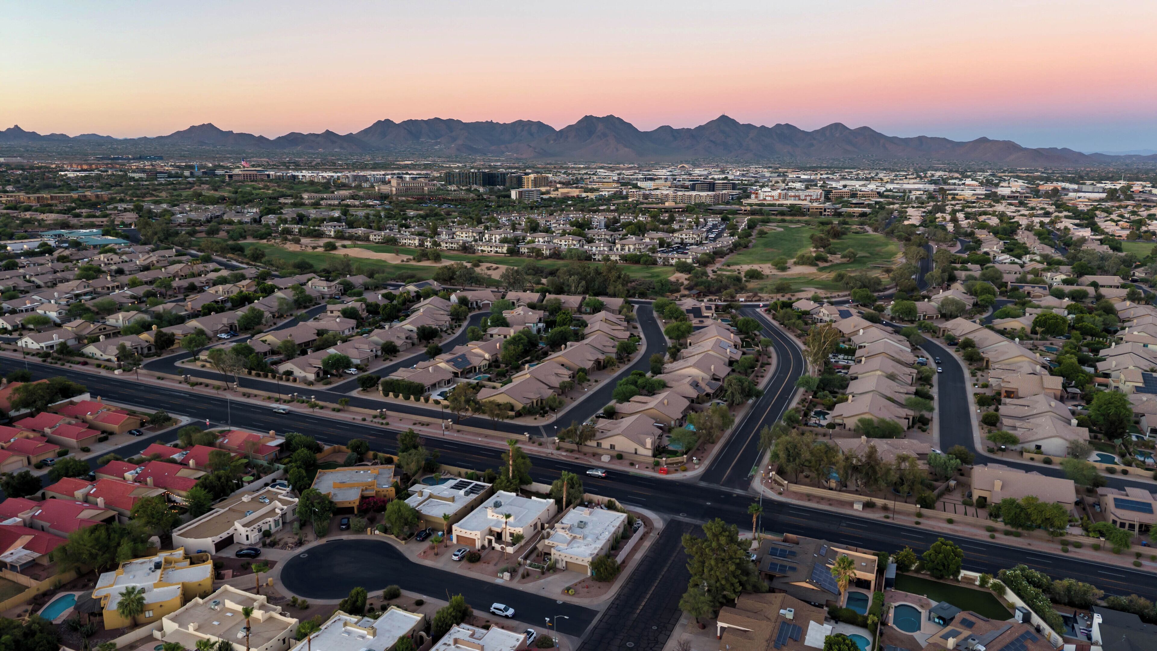 Un quartier résidentiel avec des habitations disposées de manière structurée, des routes et des montagnes qui se dessinent à l’horizon.