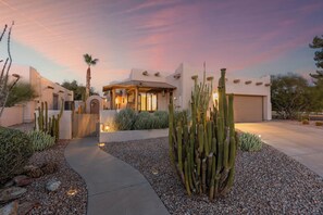 Una casa de estilo desértico con un camino que lleva a un porche techado, rodeado de cactus y plantas del desierto.
