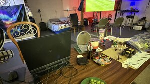Een kamer met een bed, een bureau met een computer, een televisie en verschillende spullen op het bureau.
