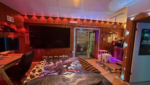 Een kamer met een bed, een bureau, een stoel, een televisie en een deur met kleurrijke verlichting.
