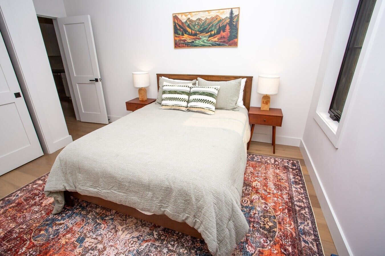 Quarto com uma cama, duas mesas de cabeceira, um criado-mudo, uma janela e um quadro na parede.