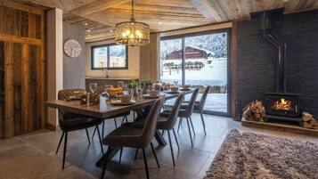 A dining area with a wooden ceiling, a chandelier, and a view of a snowy landscape through large windows.