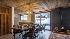 Un espace repas doté d’un plafond en bois, d’un lustre et offrant une vue sur un paysage enneigé grâce à de grandes fenêtres.