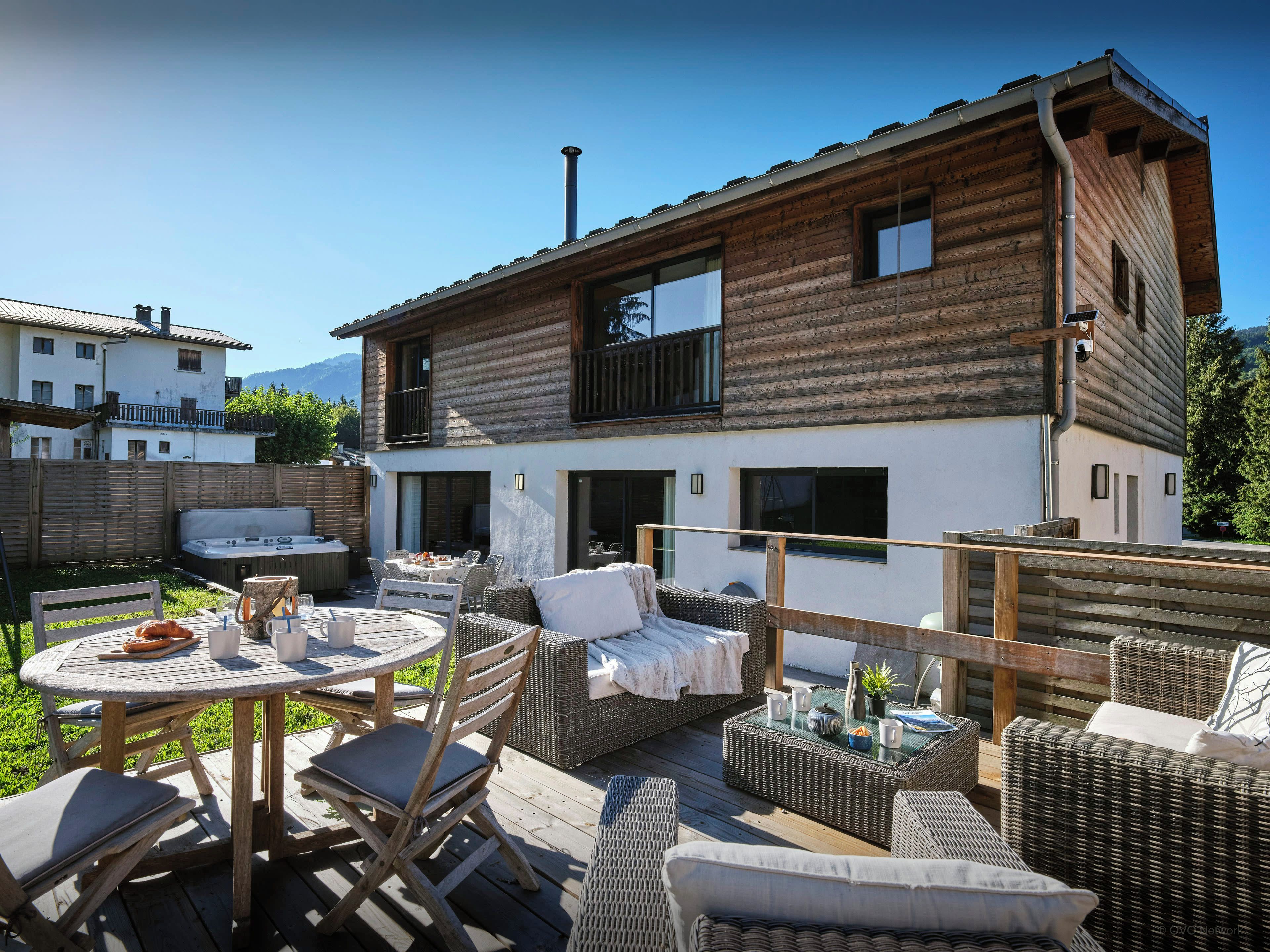 Eine Holzhütte mit einer Terrasse, die Gartenmöbel und eine Whirlwanne bietet.