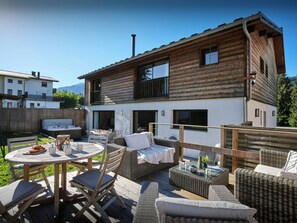 A wooden cabin with a patio area featuring outdoor furniture and a hot tub. - Chalet des Hottes - mountain break for 14 with spa - OVO Network (Verchaix)