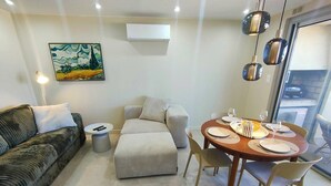 Una sala de estar moderna con sofá, reposapiés, mesa de comedor preparada para dos personas y un cuadro en la pared.