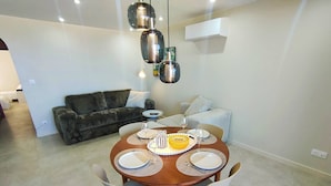 Un comedor con una mesa redonda dispuesta para cuatro personas, dos sillas blancas, un tazón amarillo y platos.