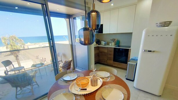 Comedor con vista a la playa, cocina moderna y refrigerador blanco.