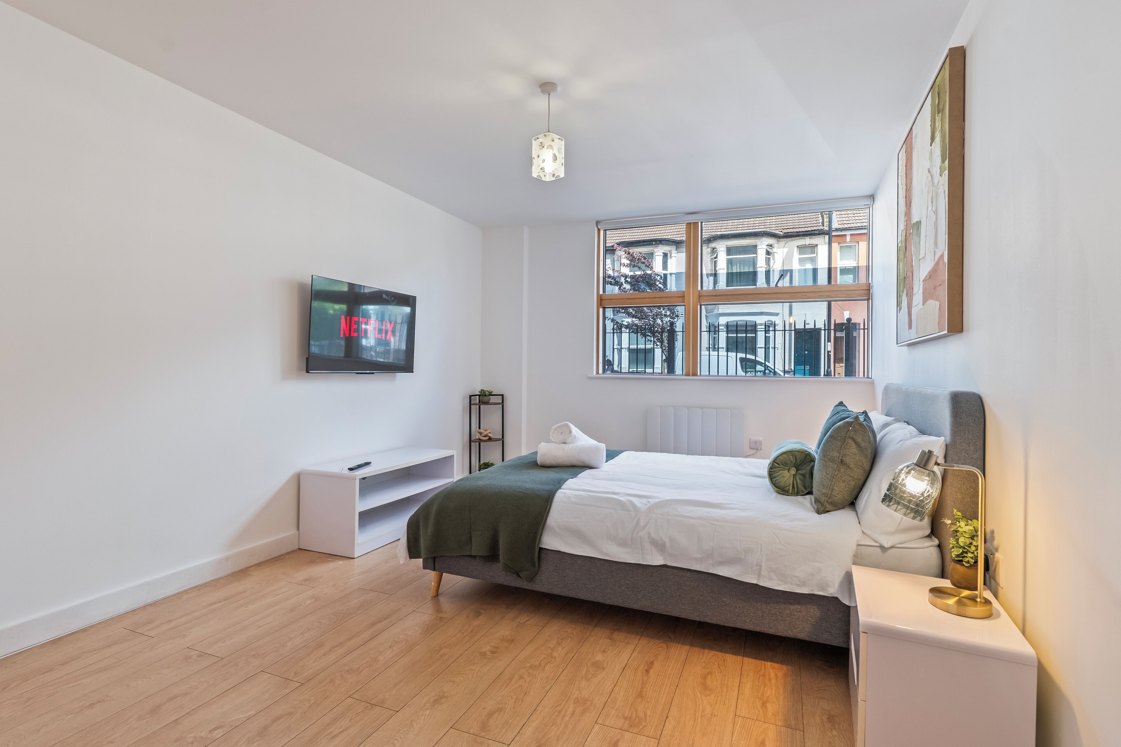 Un dormitorio moderno con una cama, un televisor, una ventana y una mesita de noche.