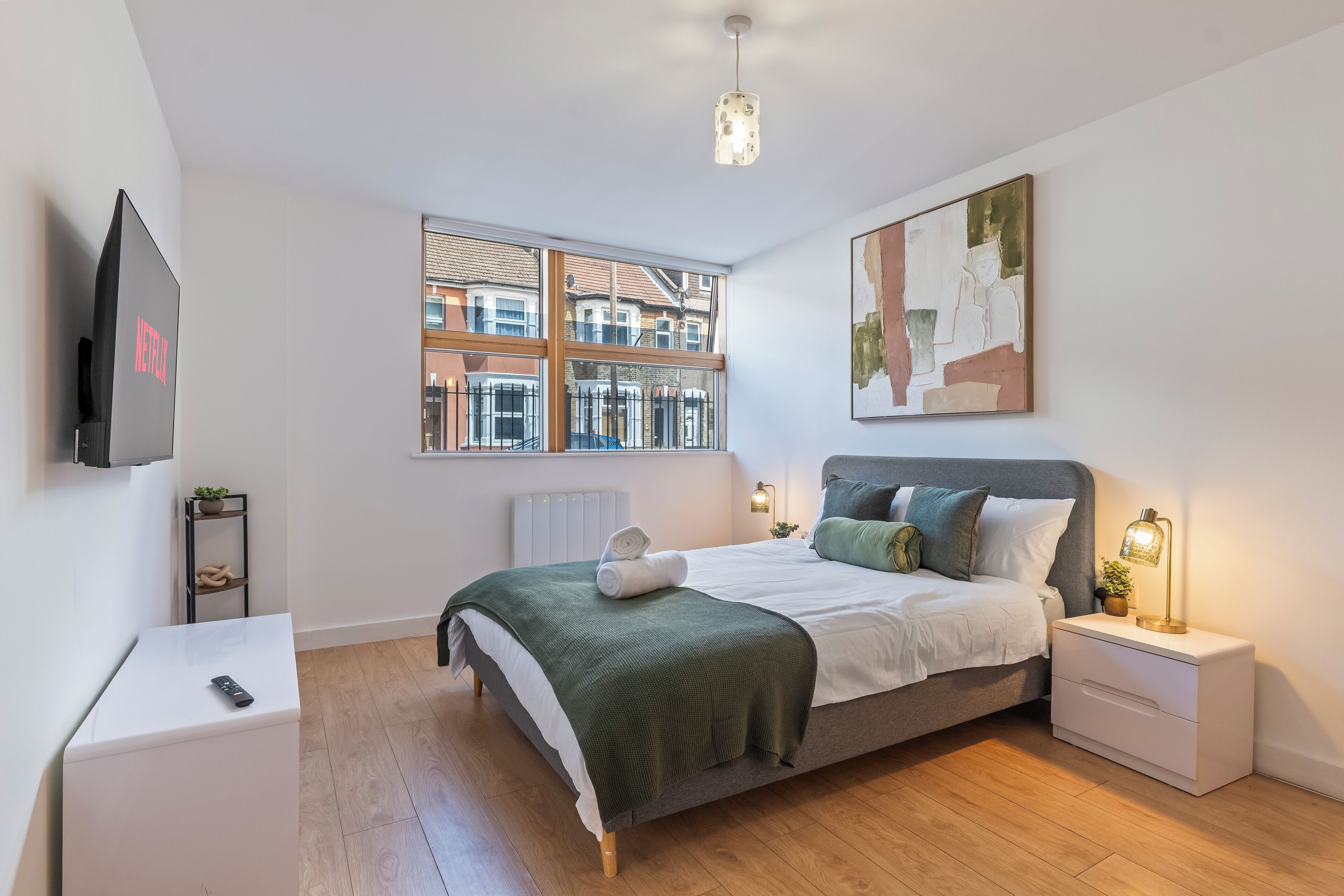 A modern bedroom with a bed, bedside tables, a TV, a window with a view, and a painting on the wall.