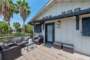 A covered outdoor seating area with wicker furniture and a wooden deck.