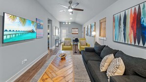 Ein geräumiges Wohnzimmer mit grauem Sofa, Holzboden und Bildern an den Wänden.
