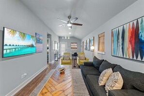 Ein geräumiges Wohnzimmer mit grauem Sofa, Holzboden und Bildern an den Wänden.