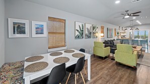 Ein modernes Wohnzimmer mit Essbereich, mit einem weißen Tisch, schwarzen Stühlen und grünen Sesseln.