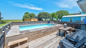 Eine Holzterrasse mit Pool, Gartenmöbeln und Blick auf die Umgebung.