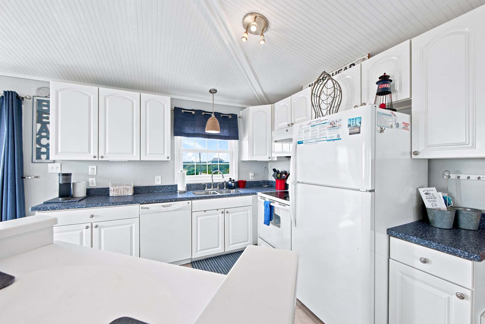 Cucina con mobili bianchi, un piano di lavoro blu, un frigorifero e una finestra con vista.