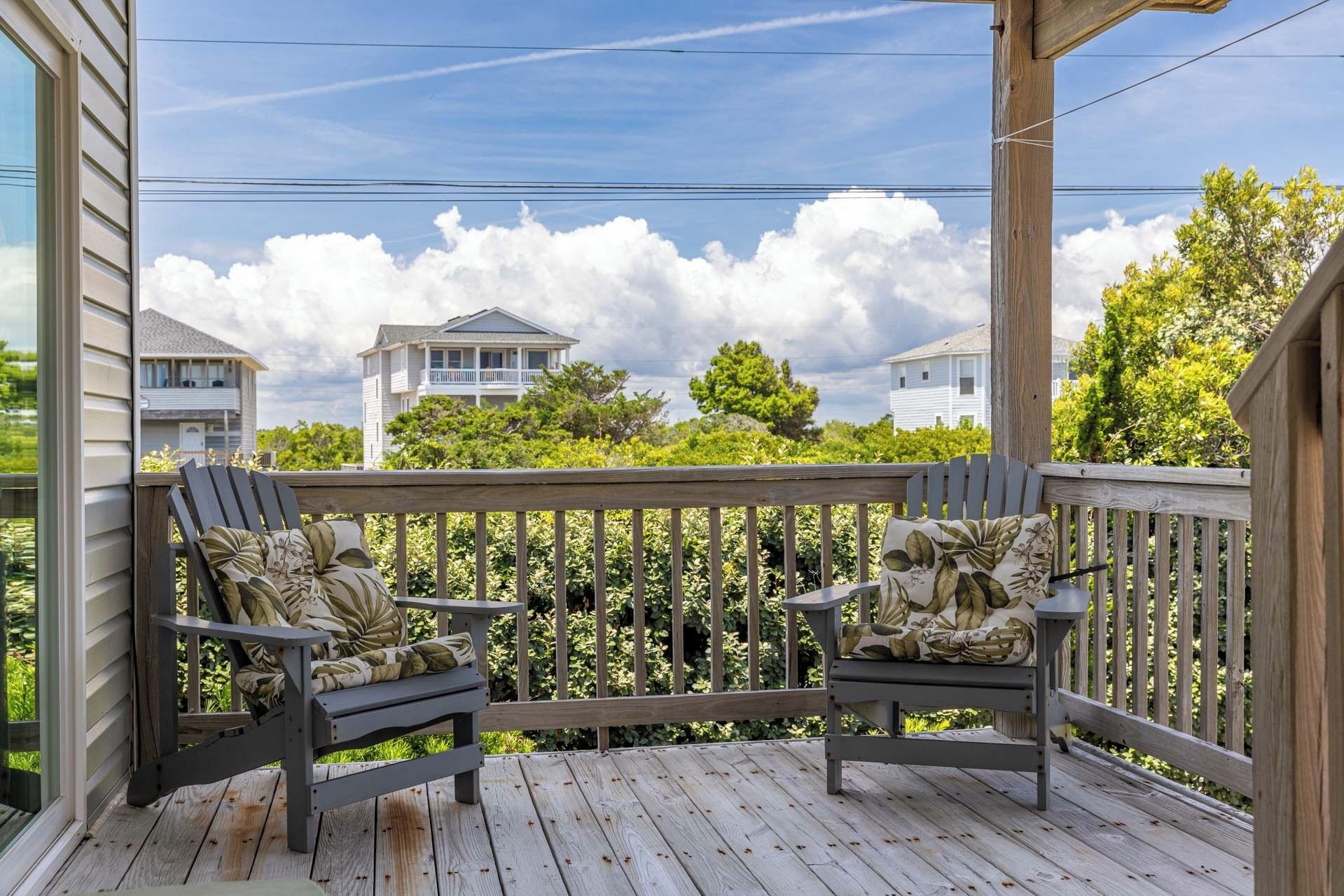 A wooden deck with two Adirondack chairs, a pergola, and a view of houses and trees.