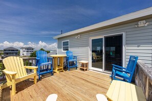 Eine Holzterrasse mit blauen und gelben Adirondack-Stühlen, einem kleinen runden Tisch und einer Glasbalkontür, die zu einem Außenbereich führt.
