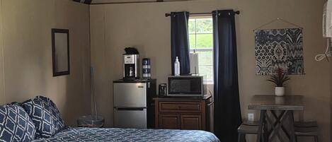 A room with two beds, a small table with chairs, a television, a refrigerator, and a window with curtains.