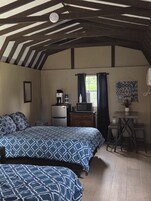 Una habitación con dos camas, una mesa pequeña con sillas, un televisor, un refrigerador y una ventana con cortinas.