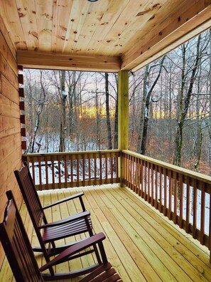 Eine Holzdielen-Terrasse mit Geländer, einer Bank und Blick auf einen verschneiten Wald.