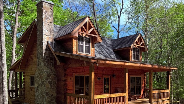 Une cabane en rondins avec une cheminée en pierre, une terrasse en bois et de nombreuses fenêtres.