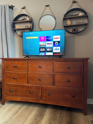 Eine hölzerne Kommode mit sechs Schubladen und ein Flachbildfernseher, der eine Roku TV-Oberfläche anzeigt.
