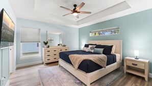 A bedroom with a bed, a nightstand, a dresser, a ceiling fan, and a window. - Simply Divine Beach Home | Walk to Beach | Firepit | Pets | Sleeps 8 (Palm Coast)