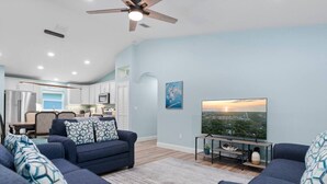 A living room with a sofa, a TV, and a view of a cityscape. - Simply Divine Beach Home | Walk to Beach | Firepit | Pets | Sleeps 8 (Palm Coast)