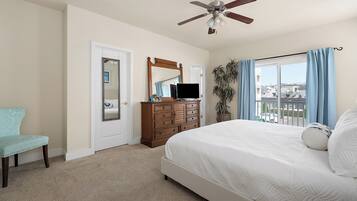 A bedroom with a bed, a dresser, a chair, a ceiling fan, a mirror, and a window with curtains.