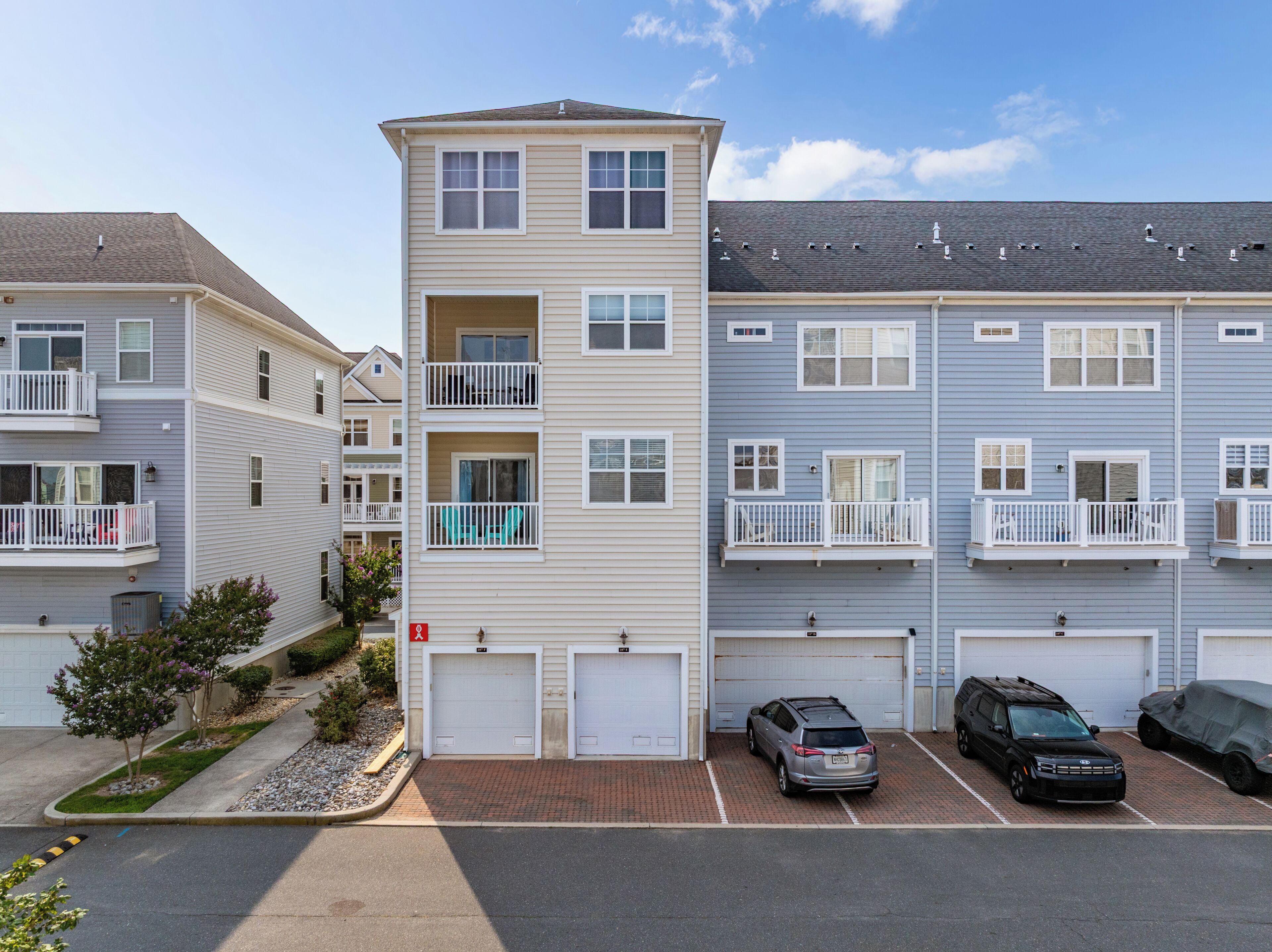 A multi-story residential building with a garage, a covered parking area, and a small garden.