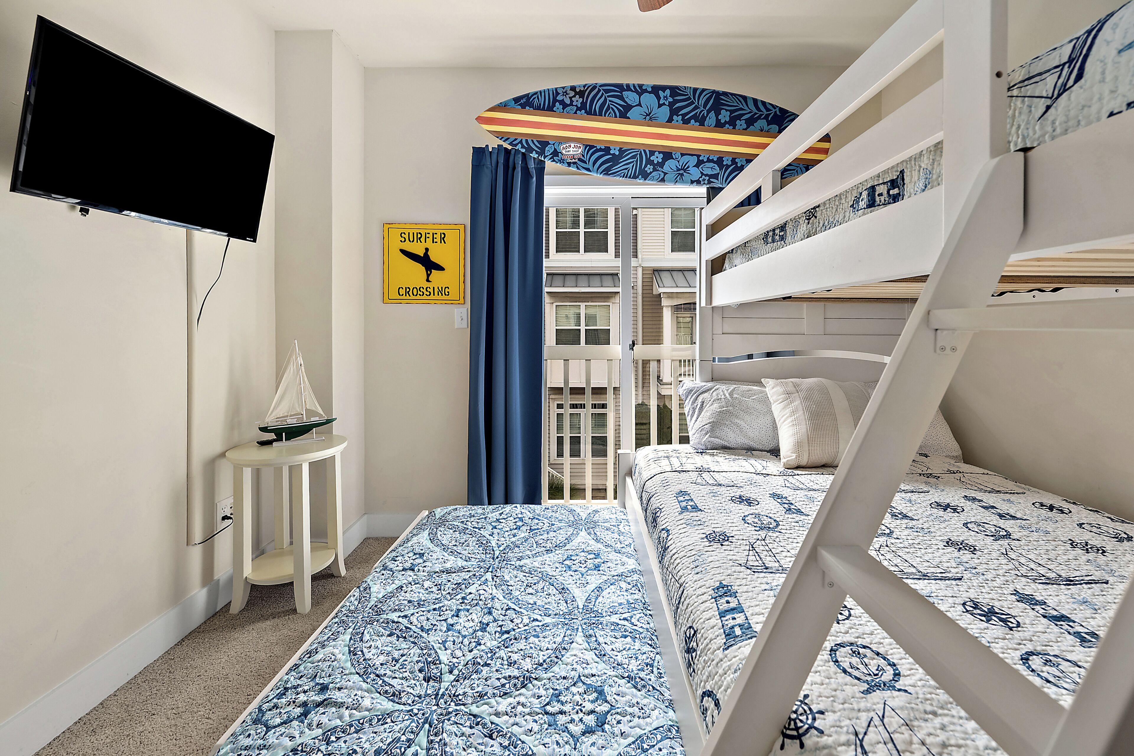 A room with bunk beds, a small table with a model sailboat, a TV mounted on the wall, and a sign indicating a surfer crossing.