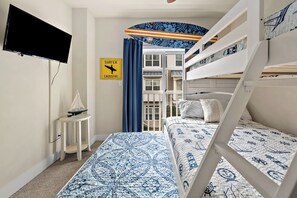Une chambre avec des lits superposés, une petite table sur laquelle est posé un modèle de voilier, un téléviseur fixé au mur et un panneau indiquant un passage pour les surfeurs.