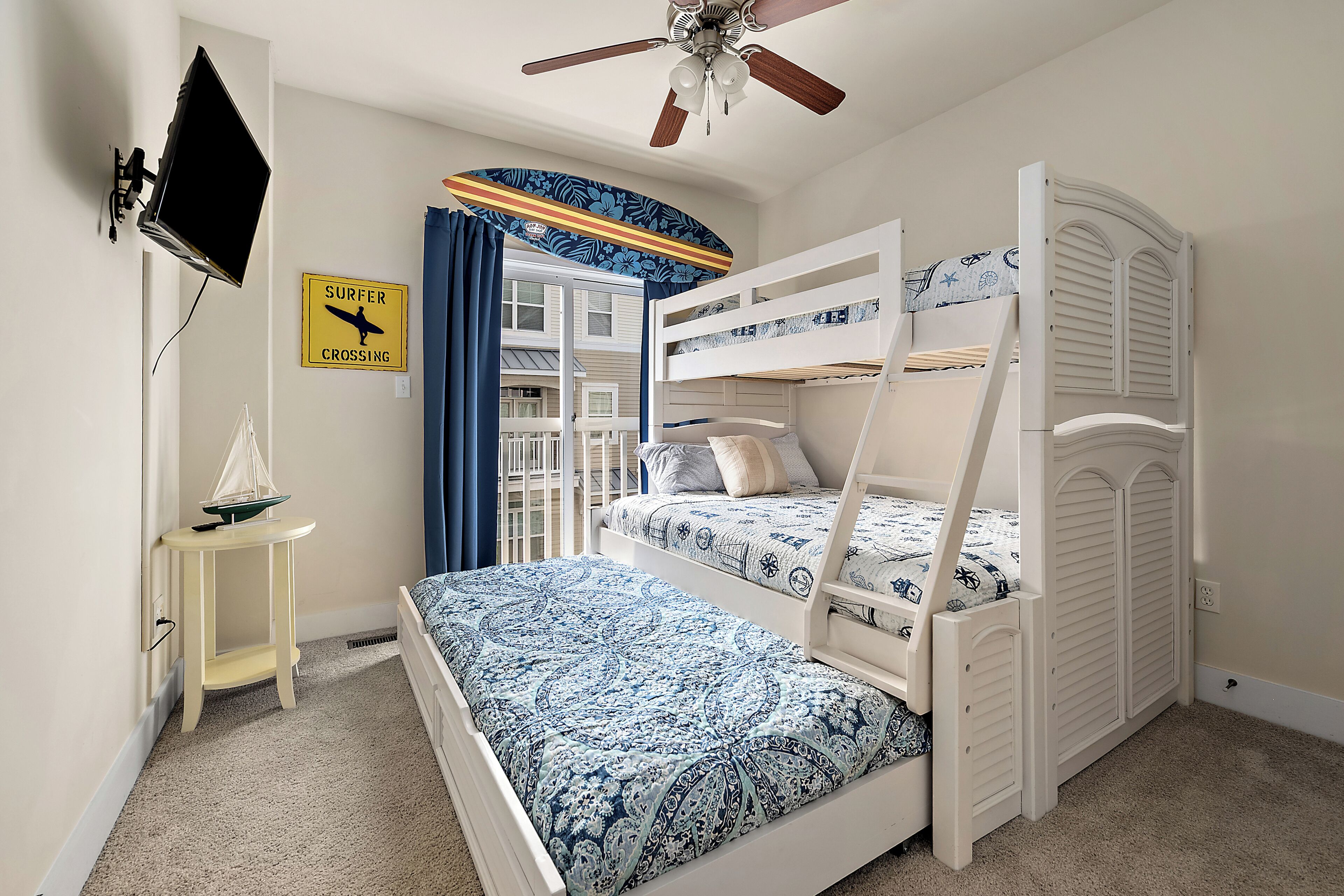 Habitación con literas, ventilador de techo, una pequeña mesa con un modelo de barco y un cartel en la pared.