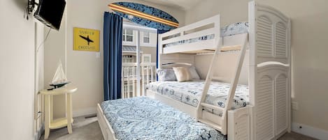 Habitación con literas, ventilador de techo, una pequeña mesa con un modelo de barco y un cartel en la pared.