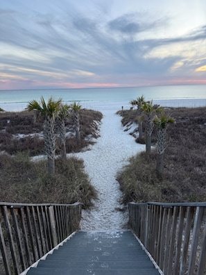 A wooden boardwalk leading to a beach with sparse vegetation and a cloudy sky. - Luxury 2-bedroom condo in Panama City Beach, few steps from the beach (Panama City Beach)