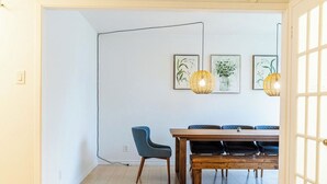 Een eetruimte met een houten tafel en stoelen, een blauwe fauteuil en drie ingelijste botanische prints aan de muur.