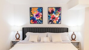 Een bed met een donker hoofdbord, twee nachtkastjes met lampen, en twee bloemschilderijen aan de muur.